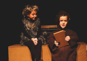 Two children sitting in dark costumes. 